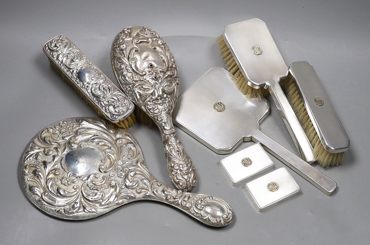 A 1970's engine turned silver three piece dressing table set, with a pair of matching jar lids, and a repousse decorated three piece dressing table set